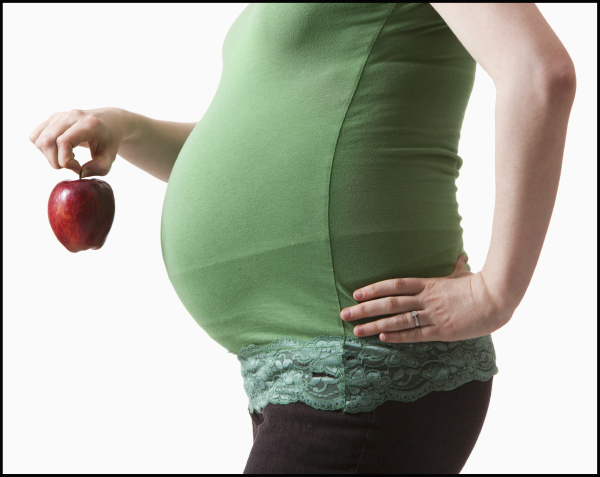 schwangere frau haelt roten apfel