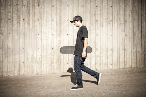 kaukasischer mann traegt skateboard in der