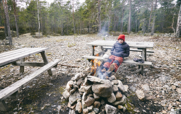 junge sitzt auf picknickbank neben lagerfeuer
