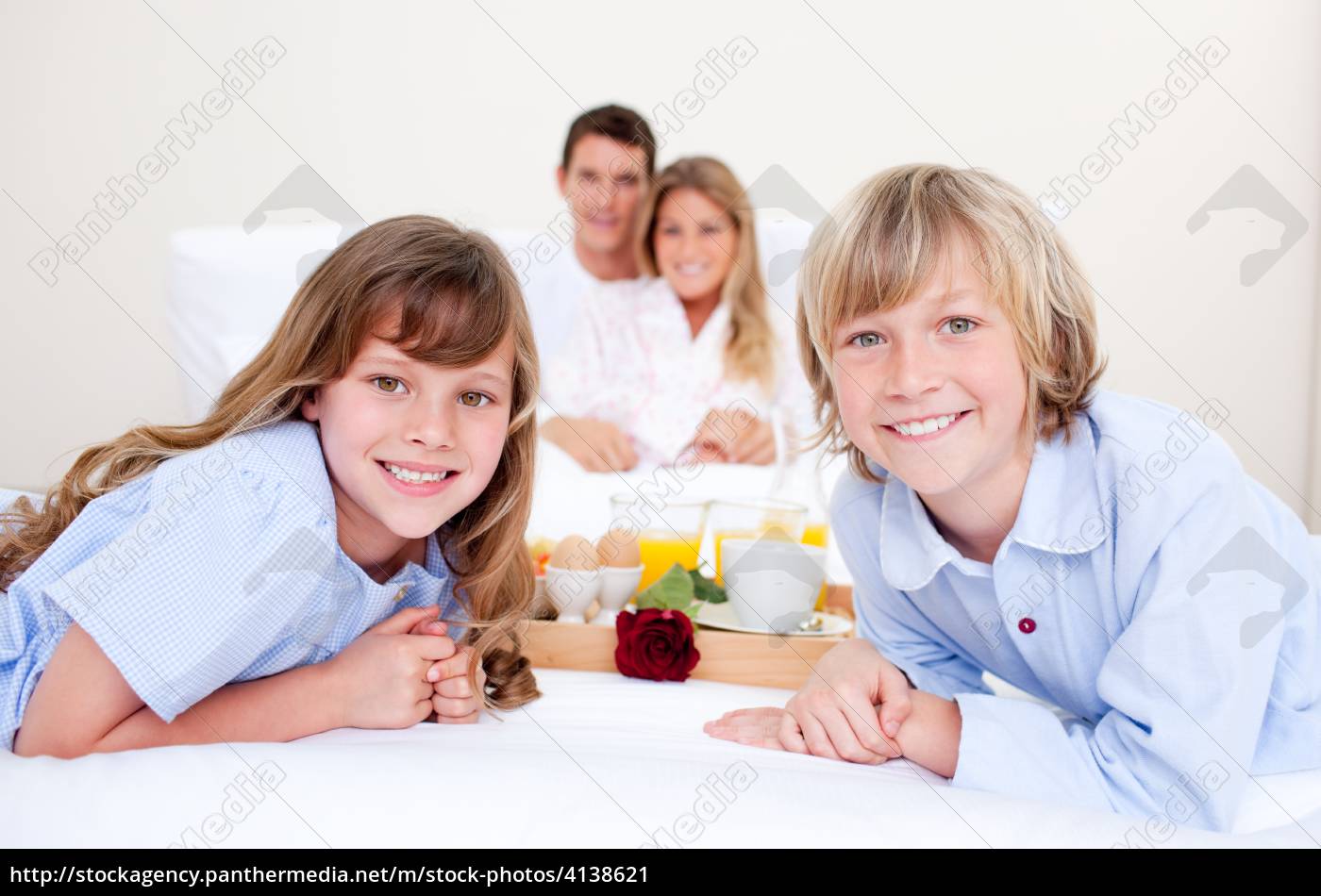 lustige familie die das frühstück sitzt auf bett isst Lizenzfreies